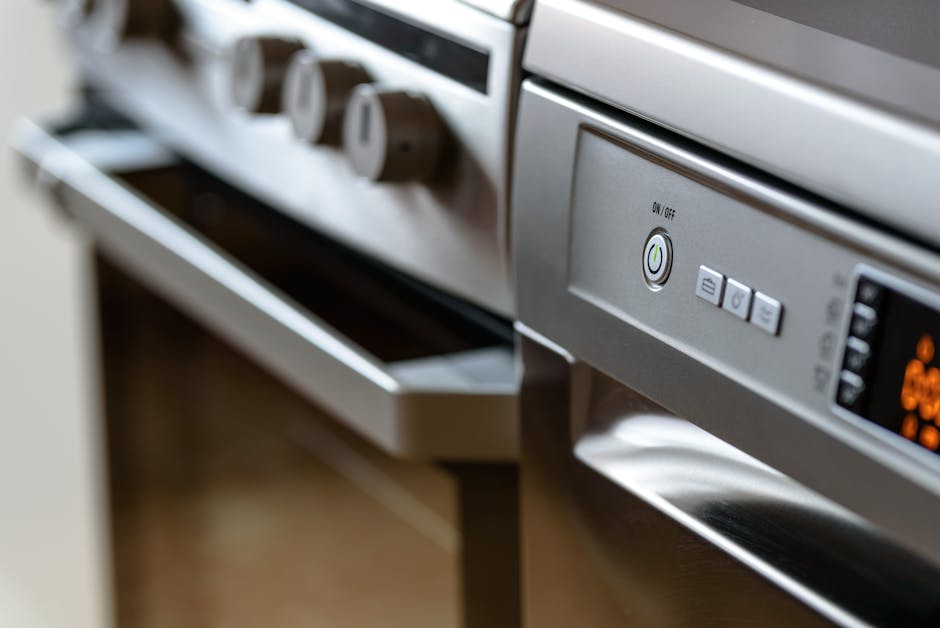 Close-up image of a white domestic gas stovetop in a kitchen, where a person wearing a blue cleaning glove and a yellow sleeve is wiping the surface with a purple microfiber cloth. The stovetop featur
