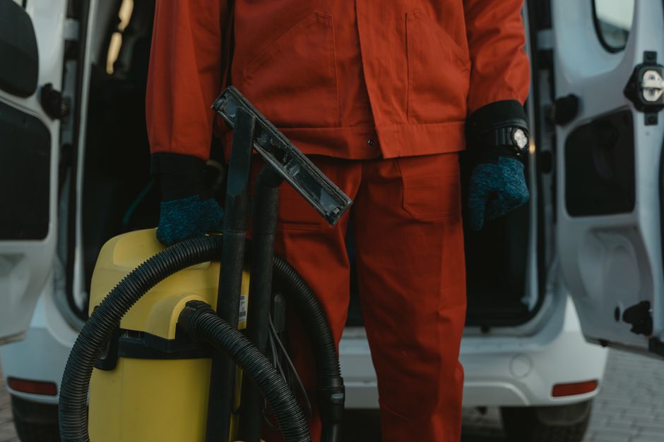 A professional cleaner from Maida Vale Cleaner is engaged in surface cleaning inside a residential kitchen. The image shows the cleaner holding a spray bottle and a cloth, preparing to wipe down surfa
